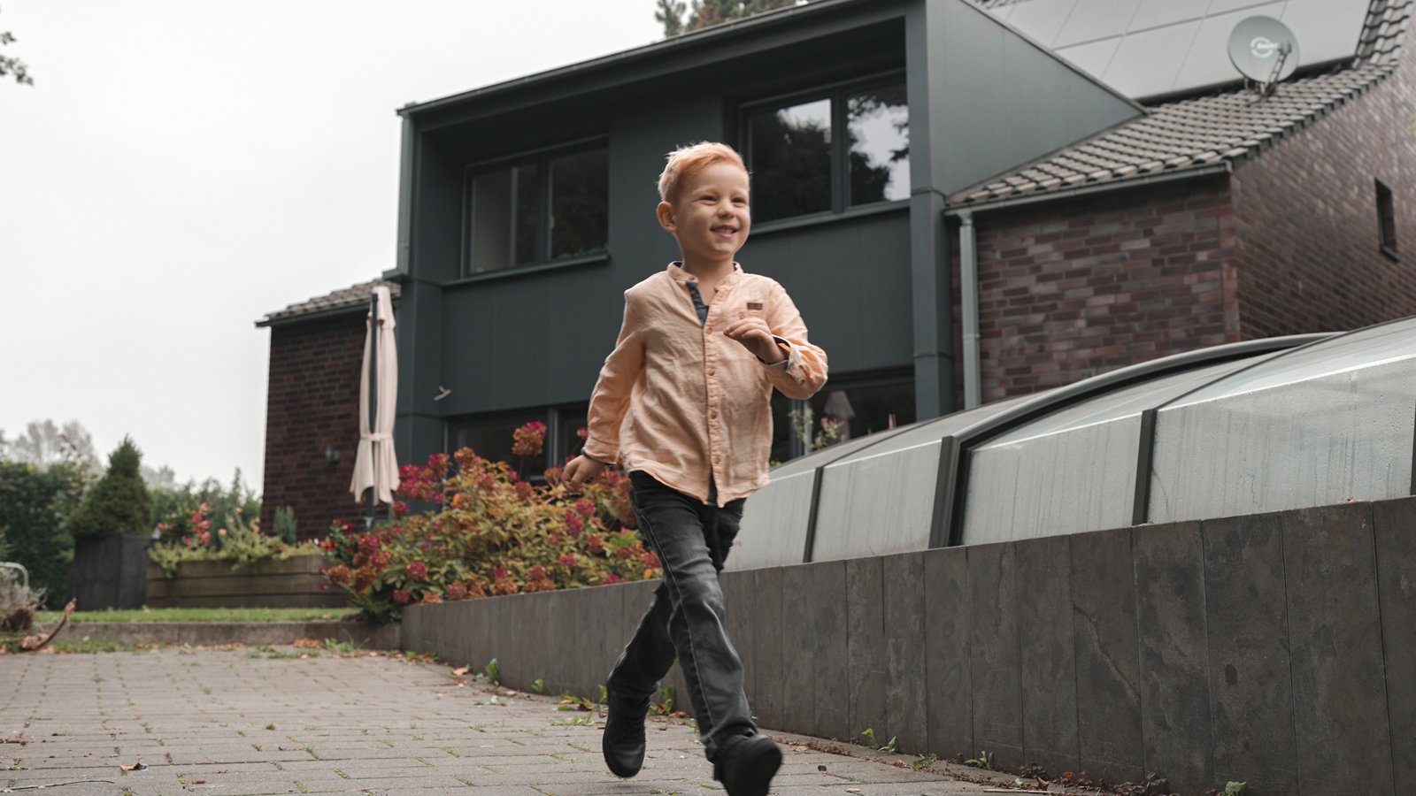 Kleiner Junge läuft lächelnd vor einem modernen Haus.