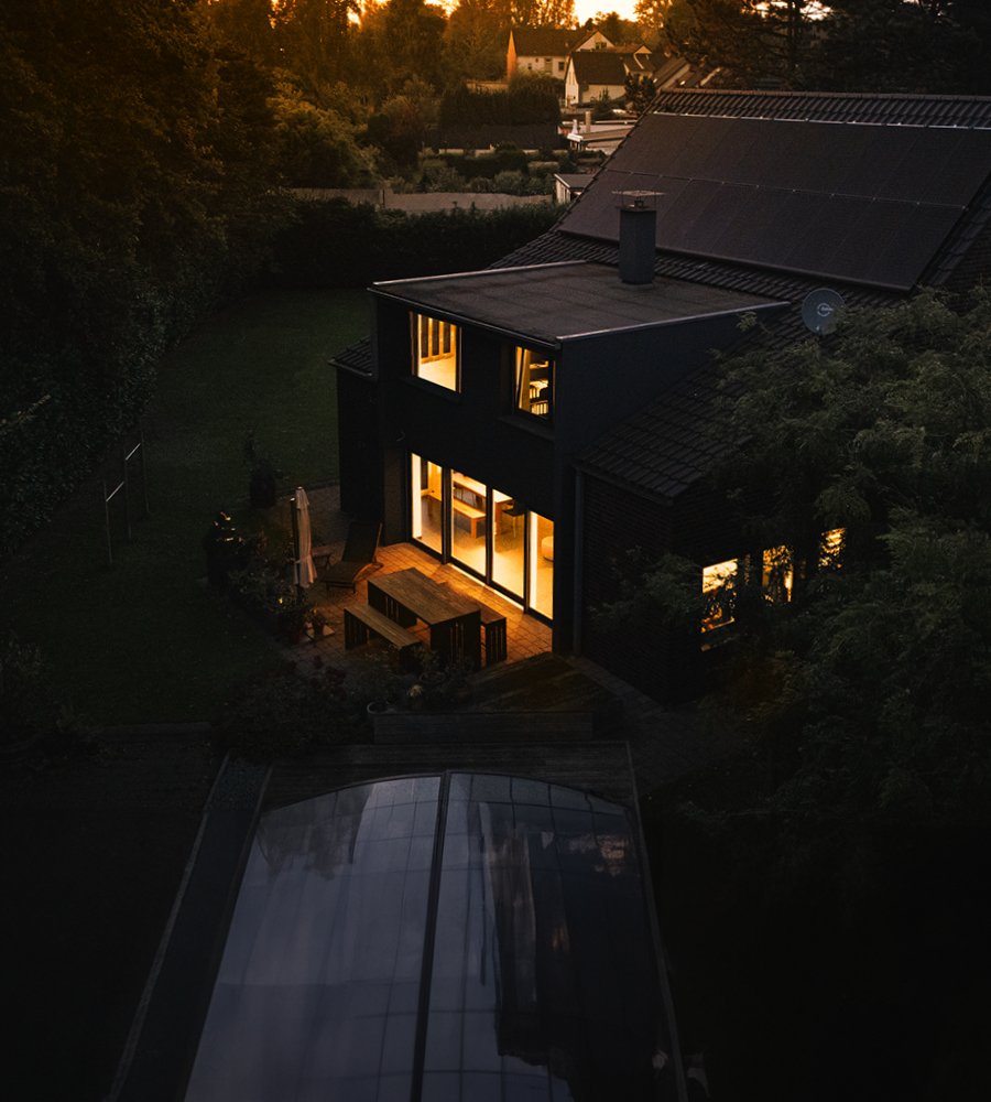 Drohnenaufnahme eines modernen Hauses am Abend mit Photovoltaik-Anlage auf dem Dach.